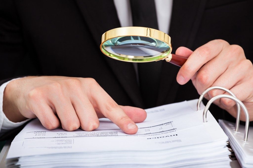 person in suit looking at a document through magnifying glass