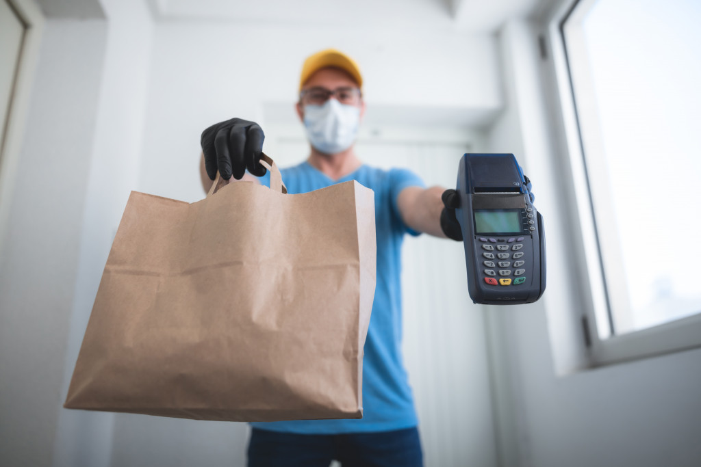 Delivery man standing at door with paper bag and payment machine
